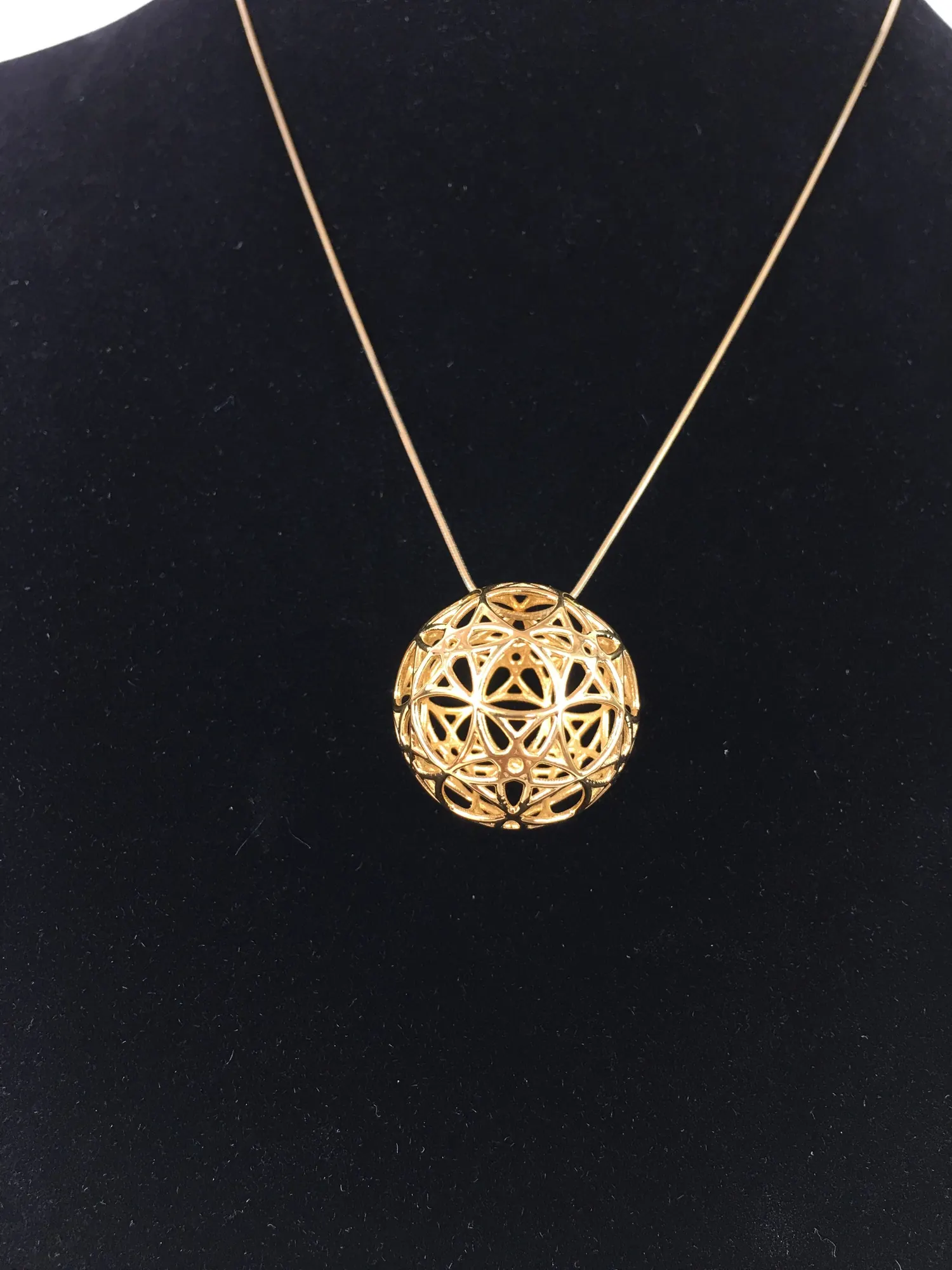 Close view of the 14k gold plated AllSphyr pendant on a chain against black fabric