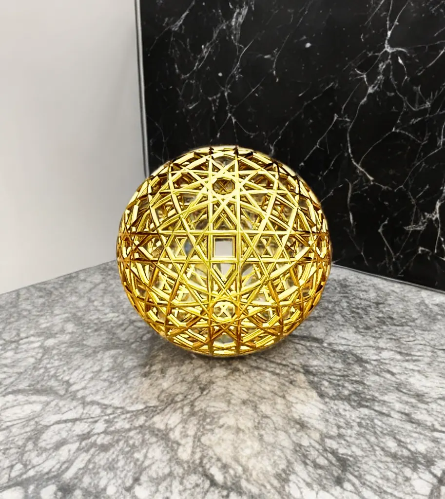 Resonance Sphyr: a gold openwork sphere of intersecting circles shown on a marble surface