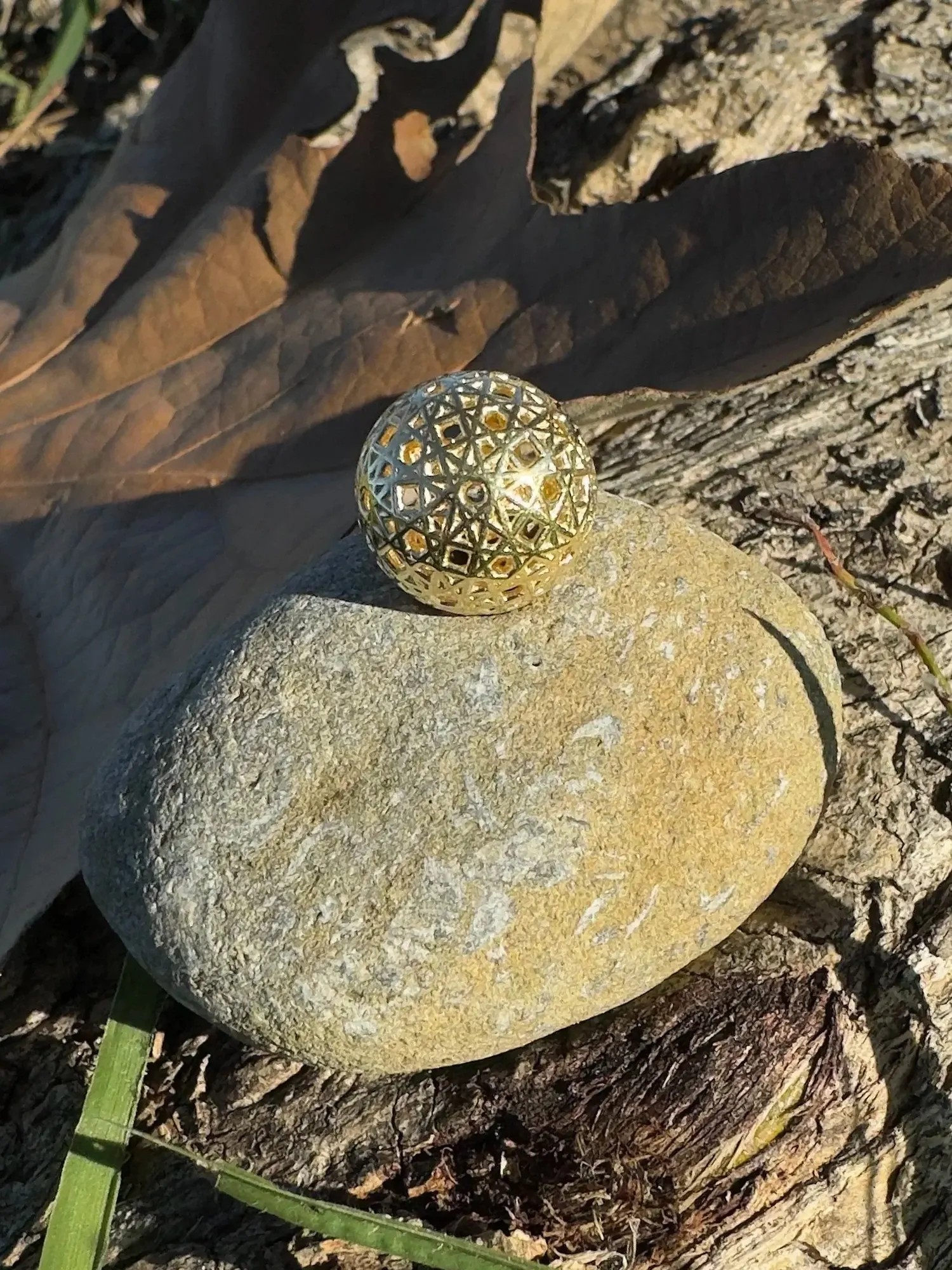 Resonance Sphyr gold pendant on a stone in dappled sunlight