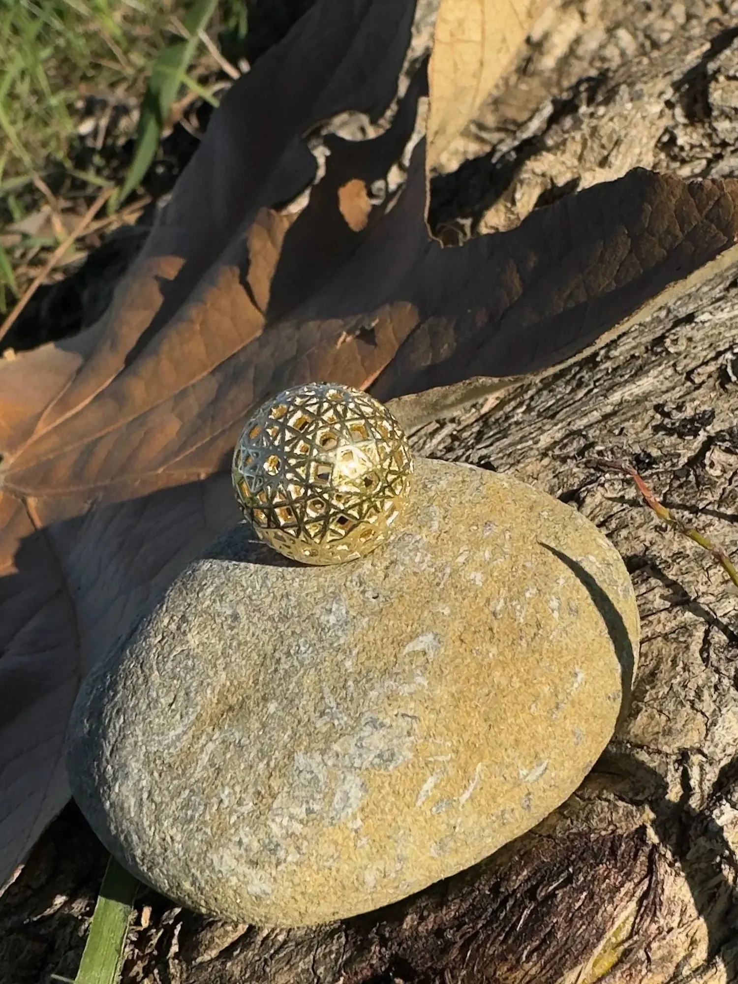 Resonance Sphyr gold pendant on a rock among leaves