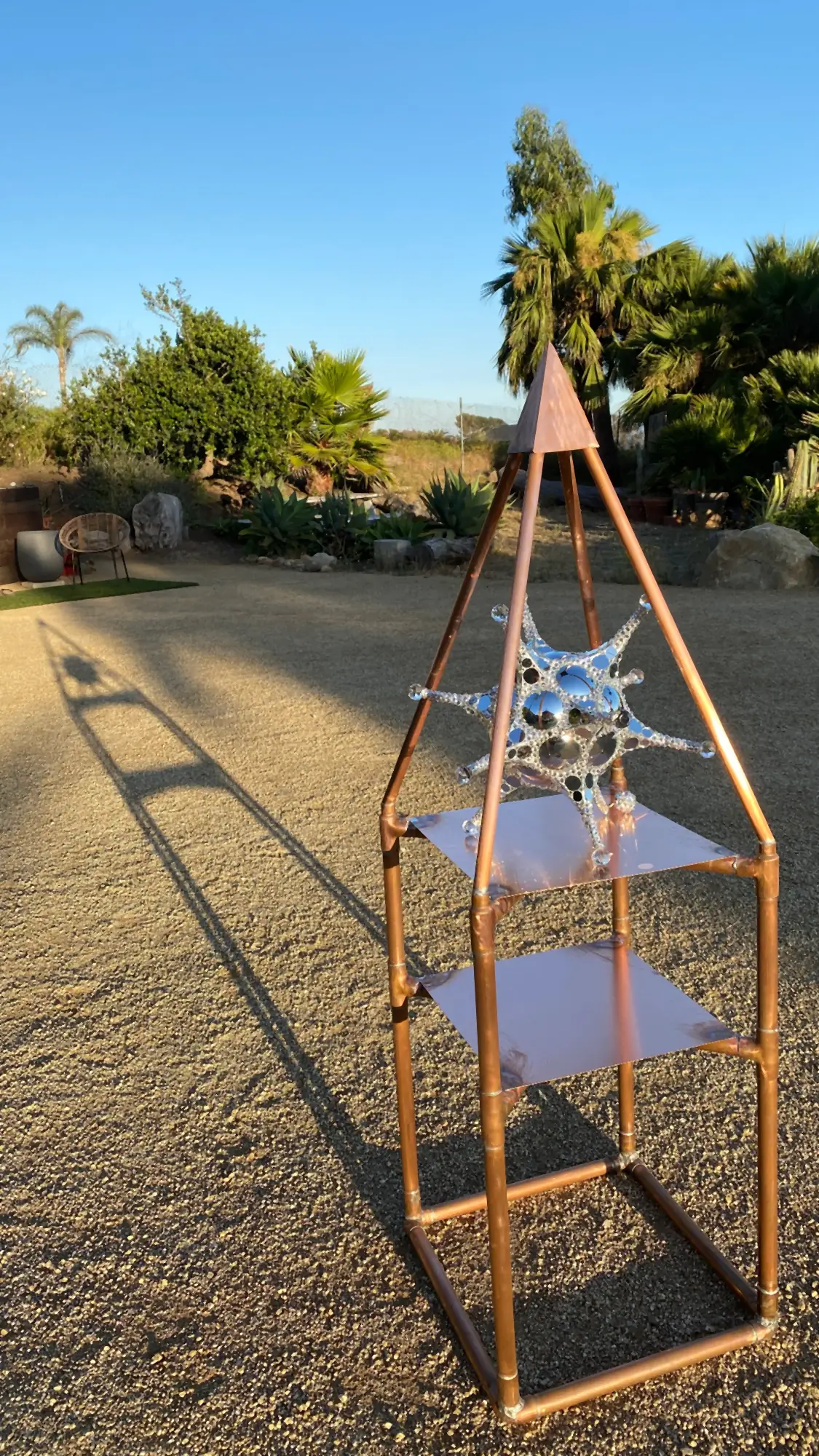 Golden Rectangle Nubian Pyramid Altar: a tall copper-tube frame with two copper shelves and a pyramid top, standing outdoors in a garden
