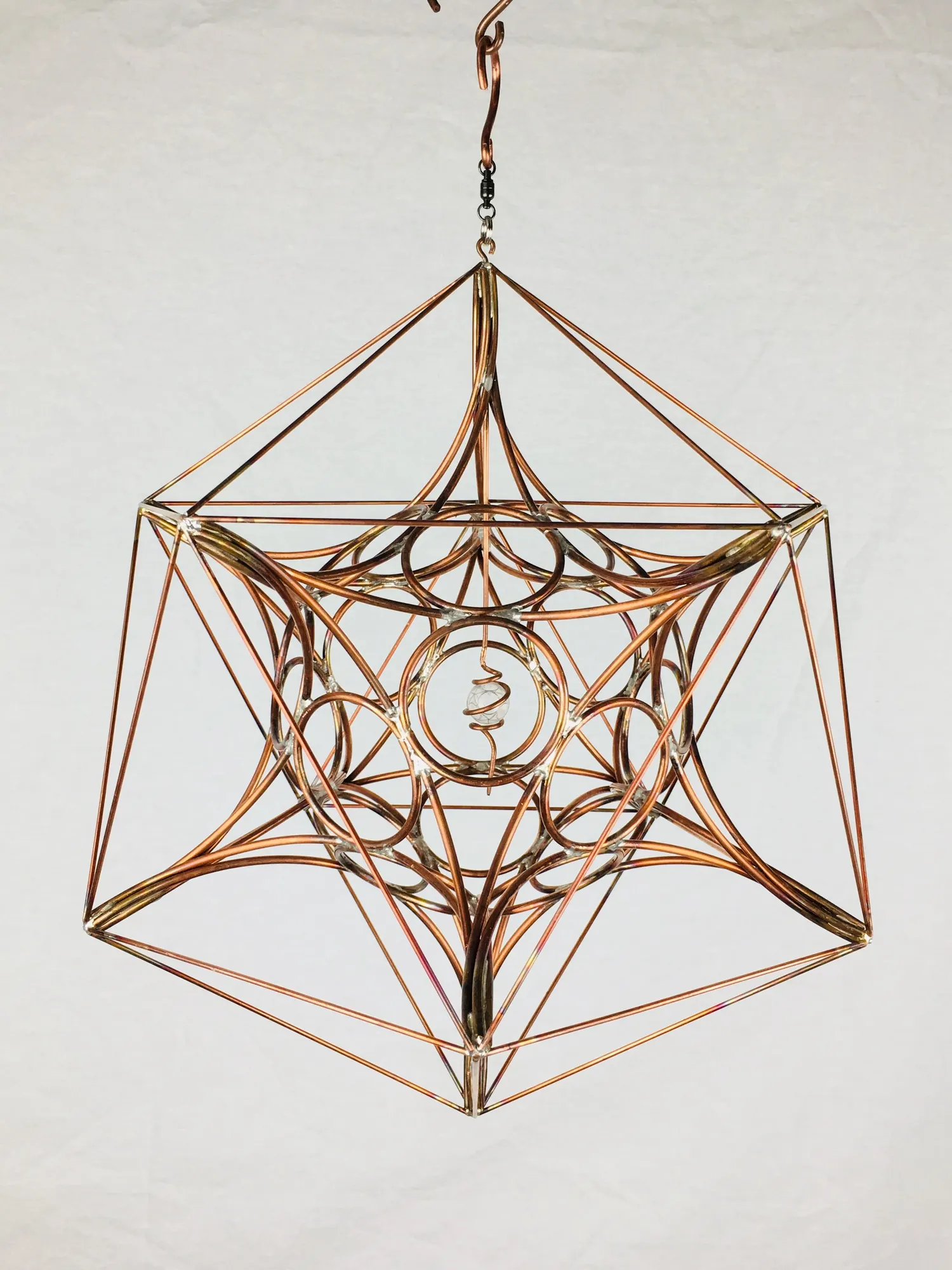 IcosaSphyr copper sculpture hanging from a hook against a white backdrop