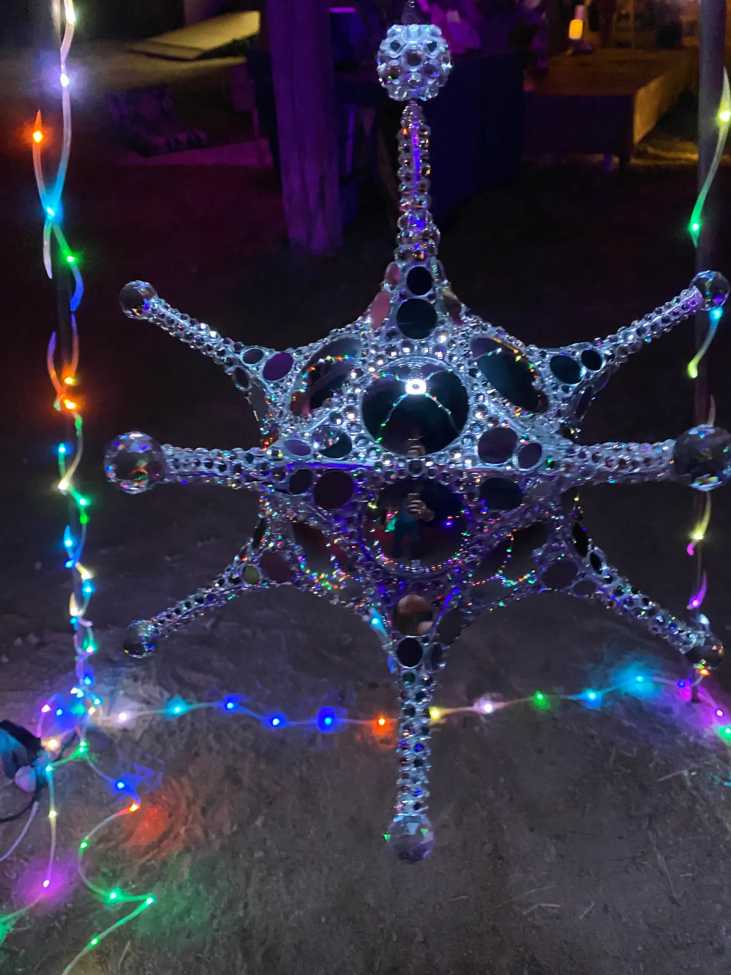 Metatron Reflections lit at night by strands of colored lights at an evening event