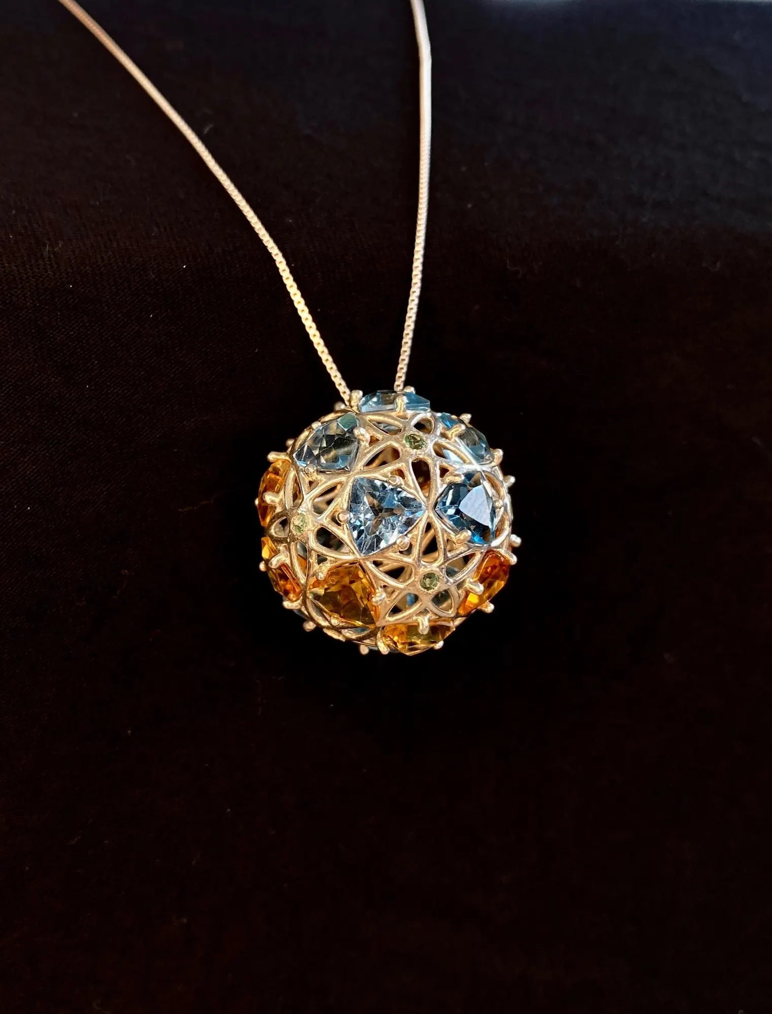 GemSphyr pendant hanging on a chain against dark fabric