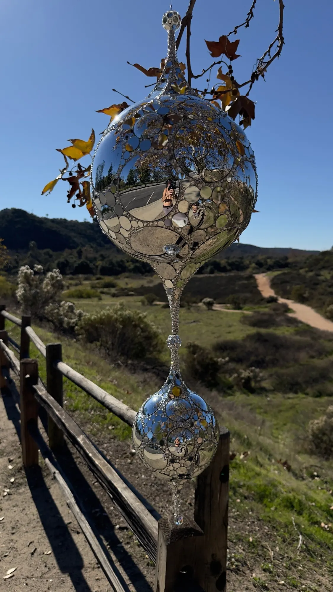 Teardrop DiscoSphyr hanging outdoors against a blue sky and hills, with a wooden fence below