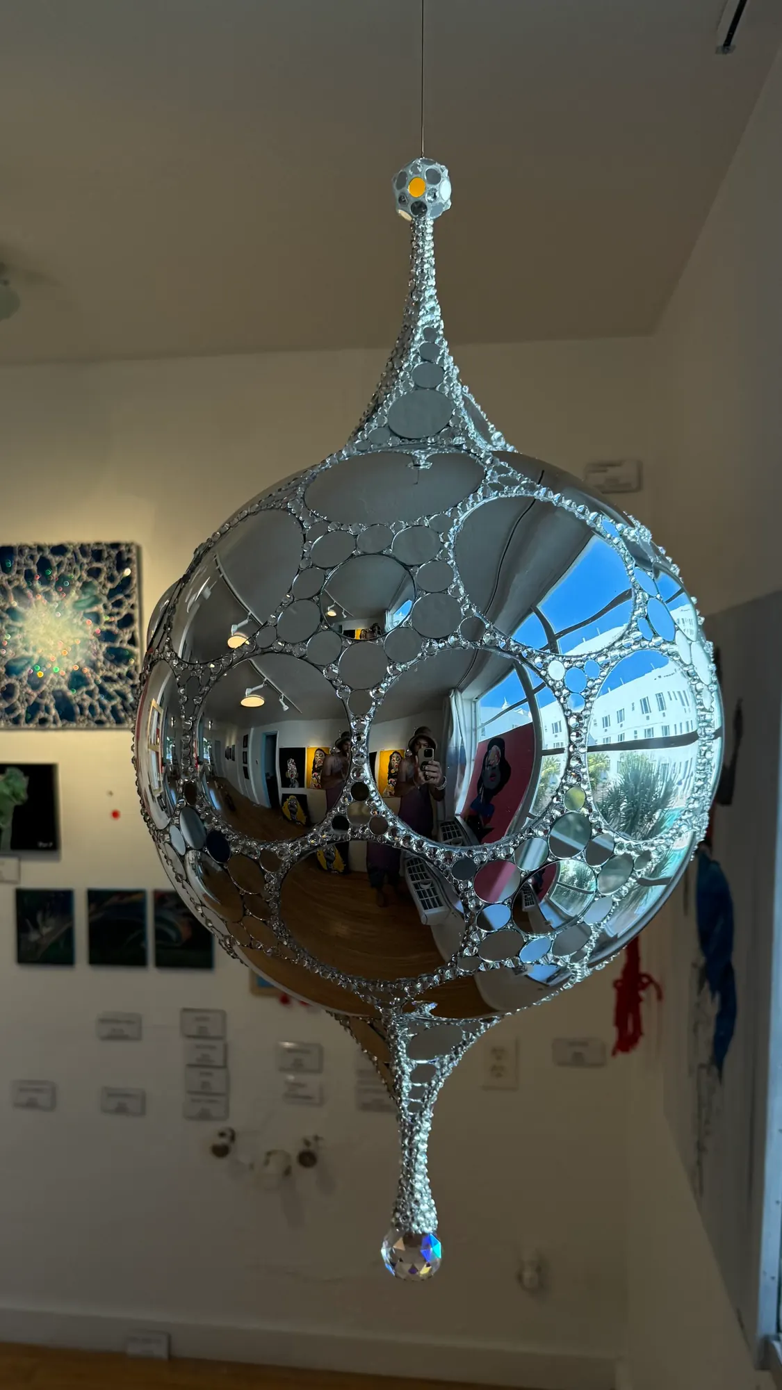 Galactic DiscoSphyr hanging near a gallery wall of paintings, with a crystal drop below