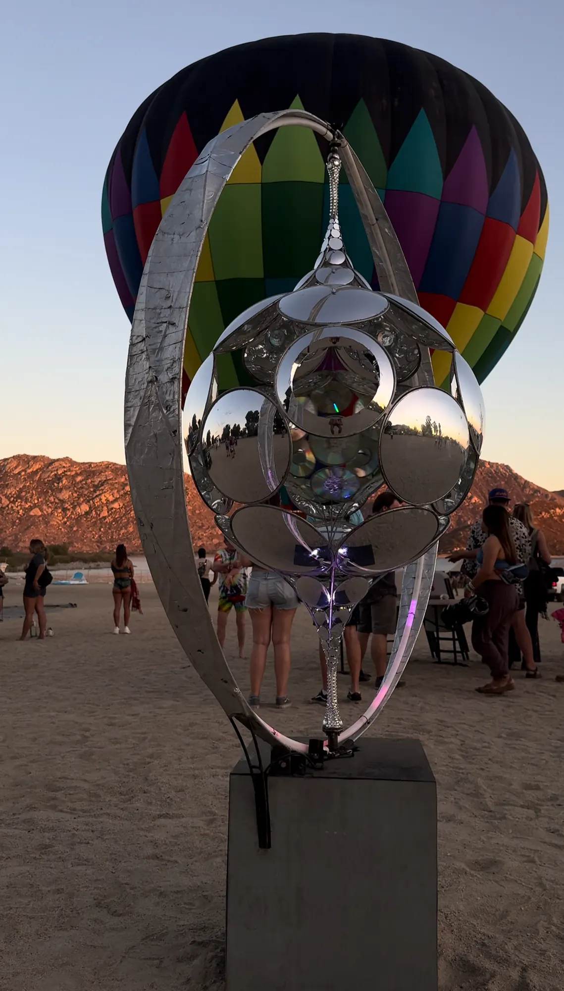 The BluRey AllSphyr, a mirrored sphere in a metal ring on a plinth at dusk, with a hot-air balloon rising behind it