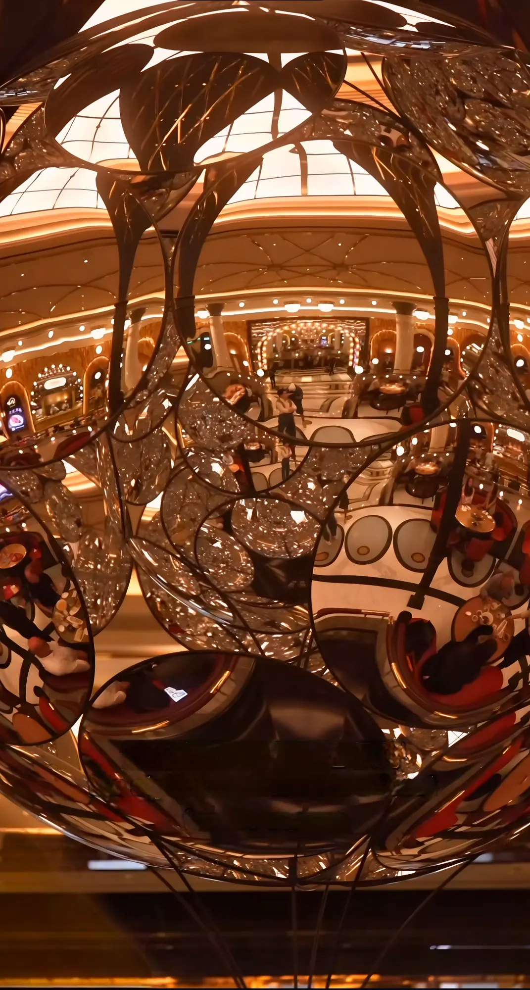 Close view of a mirrored sphere suspended beneath a bronze palm-frond canopy, its facets reflecting the dining room below